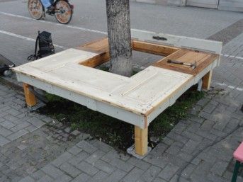 Eine um einen Baum herum gebaute Holzbank im städtischen Umfeld. 
