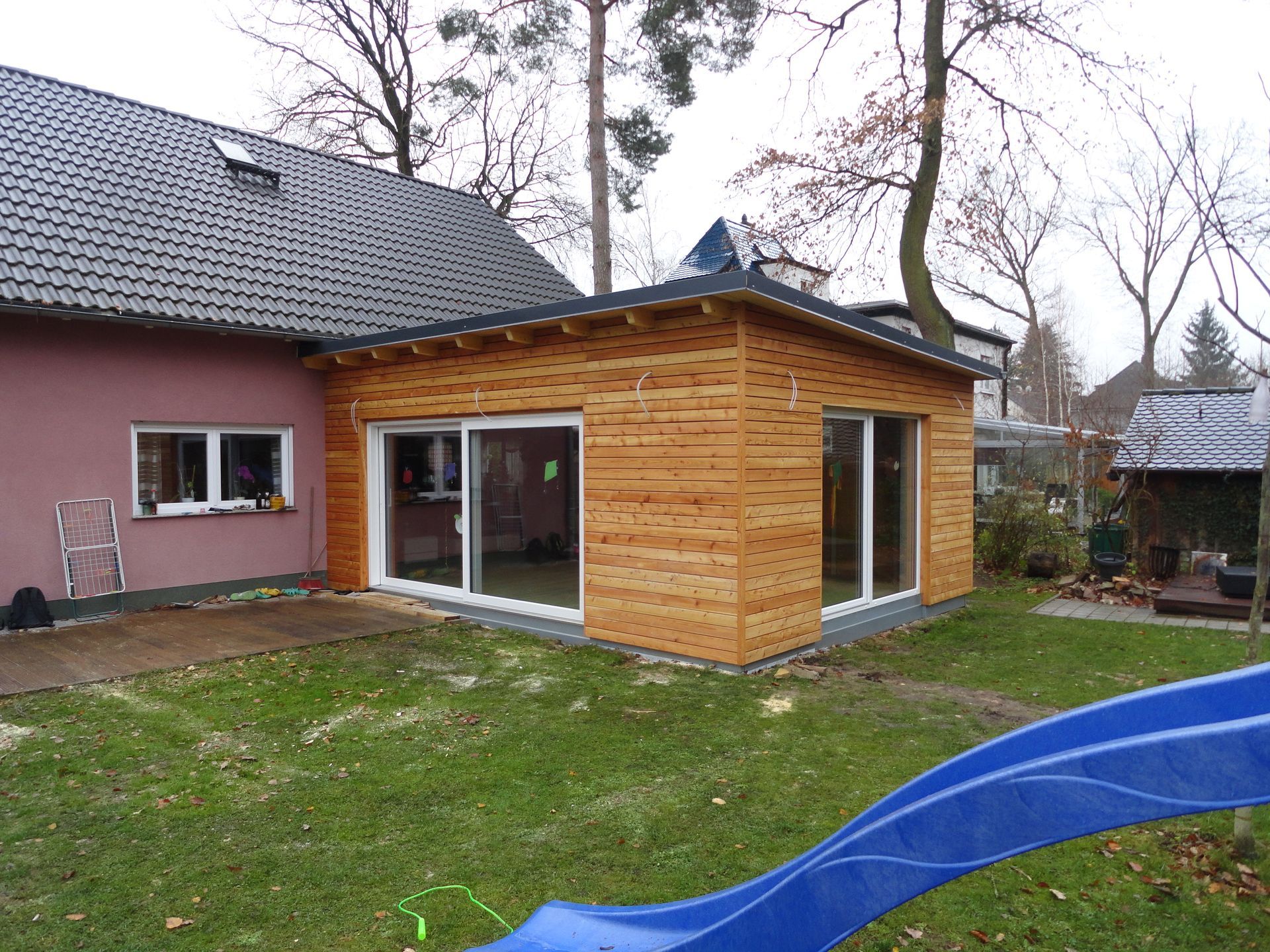 Holzanbau eines rosafarbenen Hauses mit großem Wintergarten.