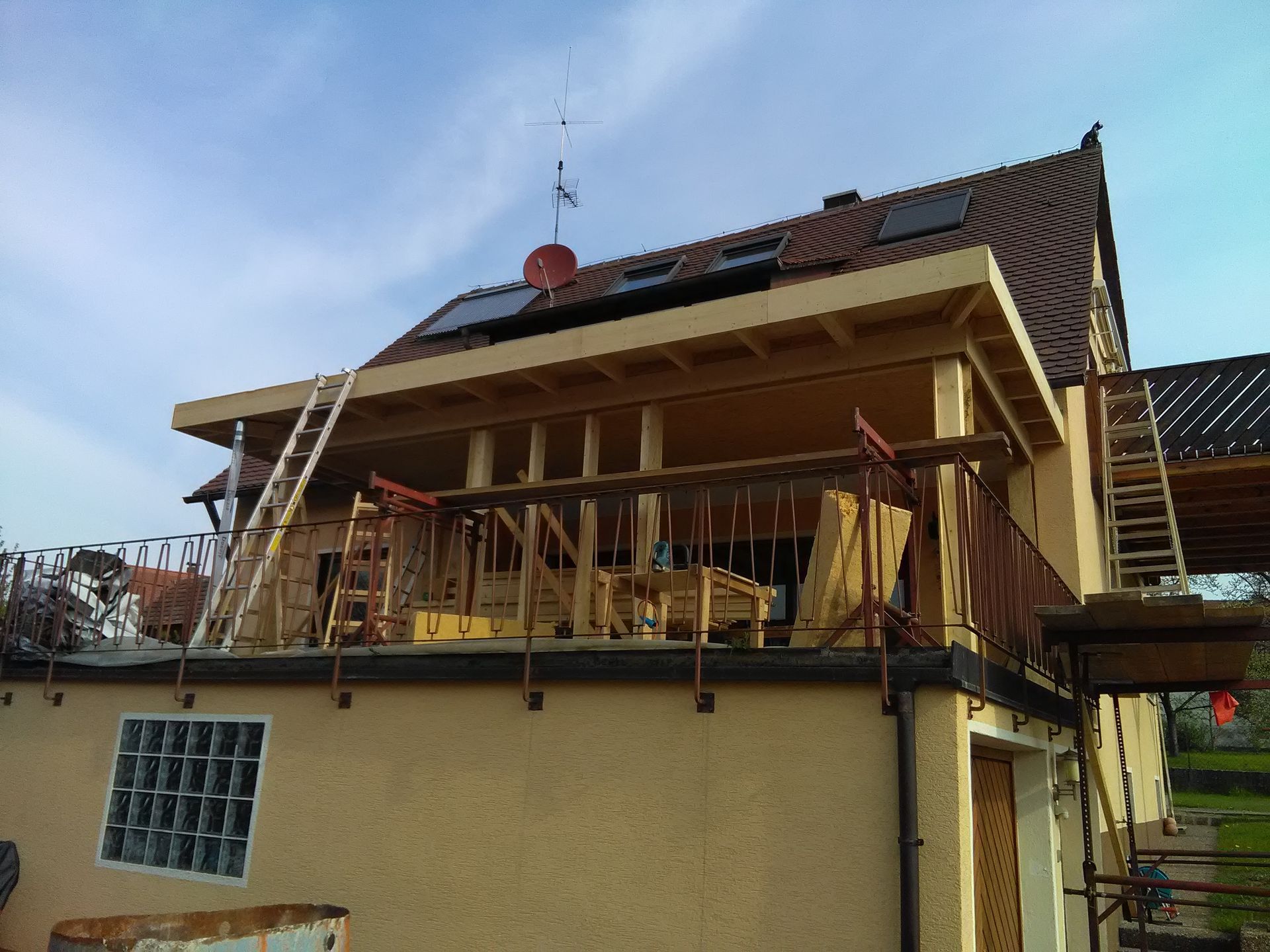 Bau eines Anbaus an ein Gebäude mit Balkon. Holzkonstruktion, Leitern und Gerüste sind zu sehen.