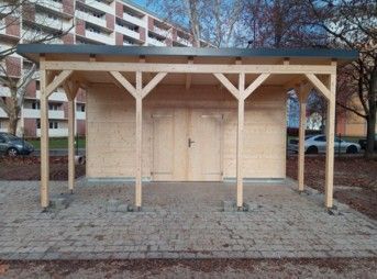 Ein Holzschuppen mit überdachtem Eingang auf gepflasterter Fläche.