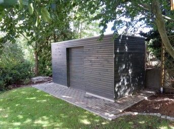 Ein moderner, grauer Holzschuppen mit Schiebetür in einem Garten auf einer gepflasterten Fläche.