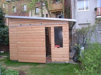 Holzschuppen mit Schiebetür und Fenster in einem grasbewachsenen Hinterhof.