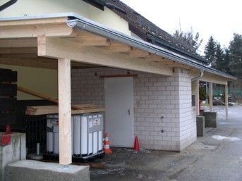 Carport mit weißen Ziegelwänden, Holzbalken und weißer Tür. 