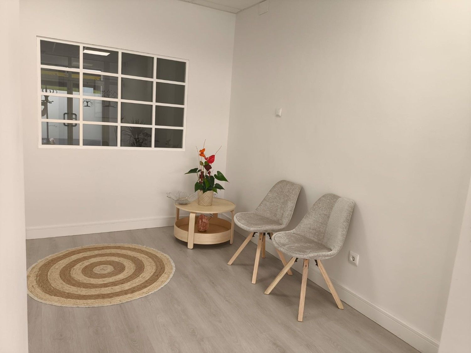 Una sala de espera con dos sillas grises, una pequeña mesa de madera 