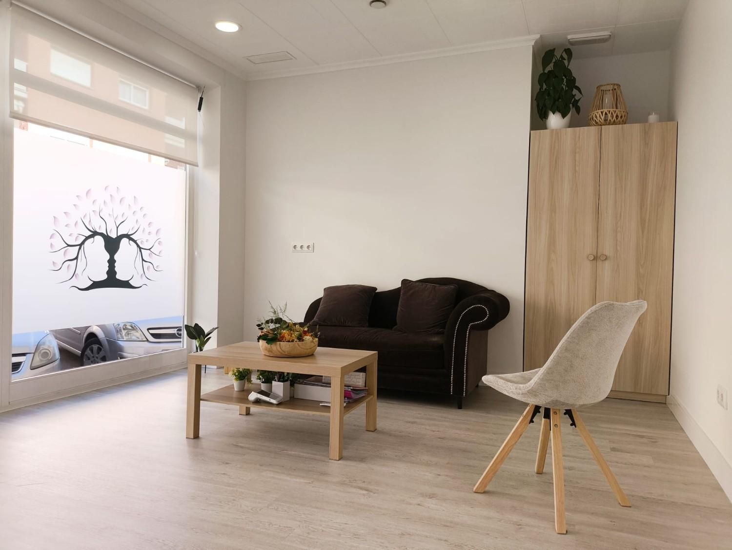 Una oficina luminosa con un sofá oscuro, una mesa de centro de madera clara,