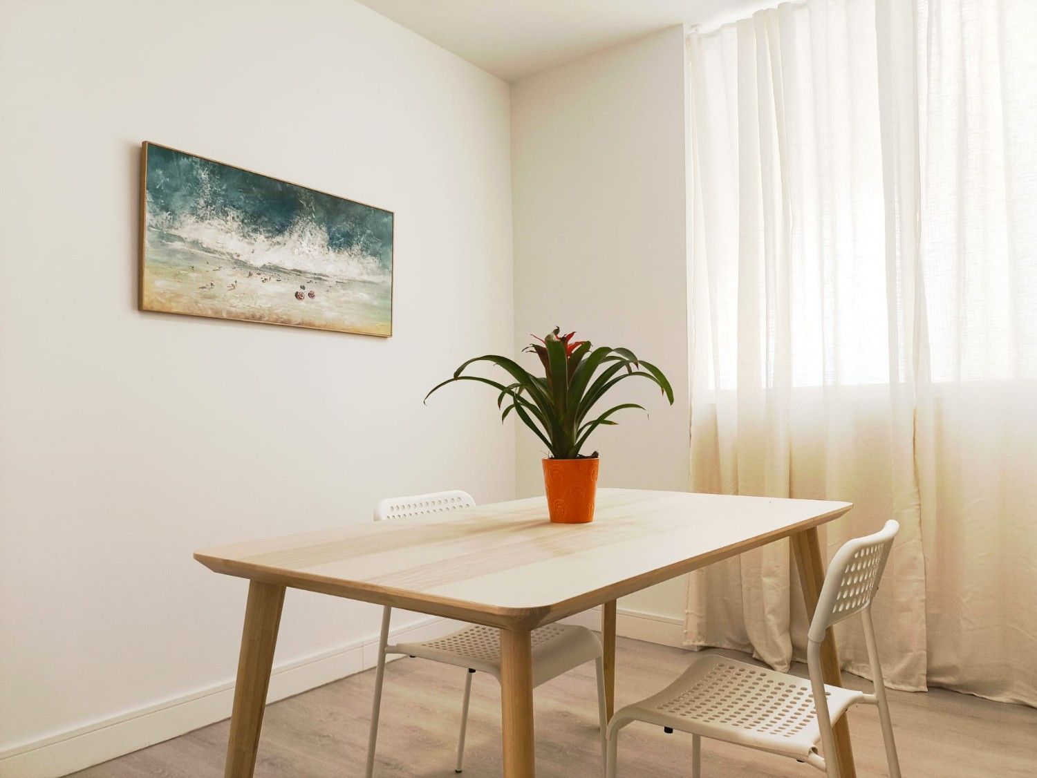 Una mesa de comedor de madera clara con una planta en maceta
