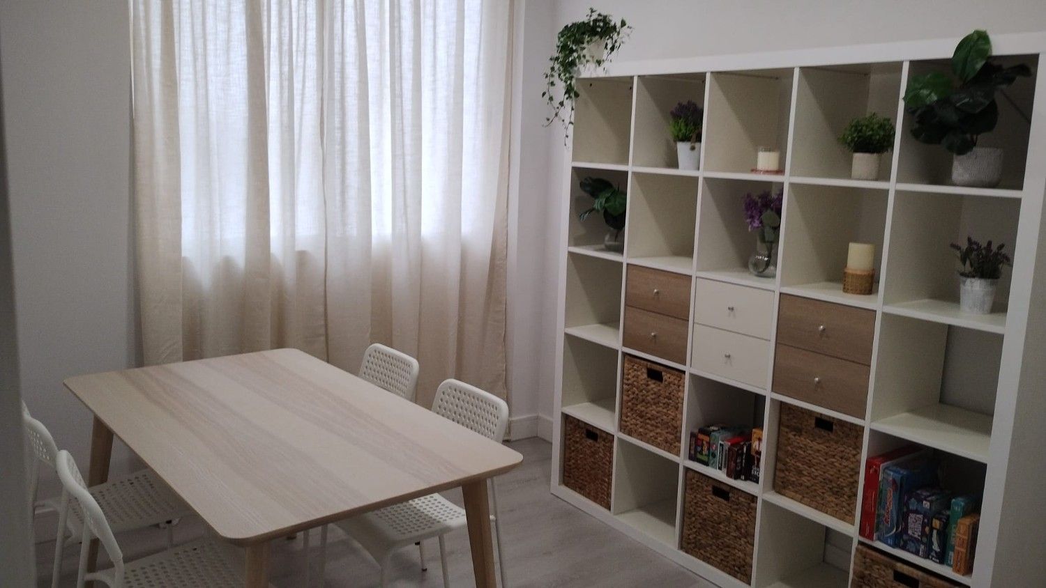 Una habitación con una mesa de madera clara, cuatro sillas blancas