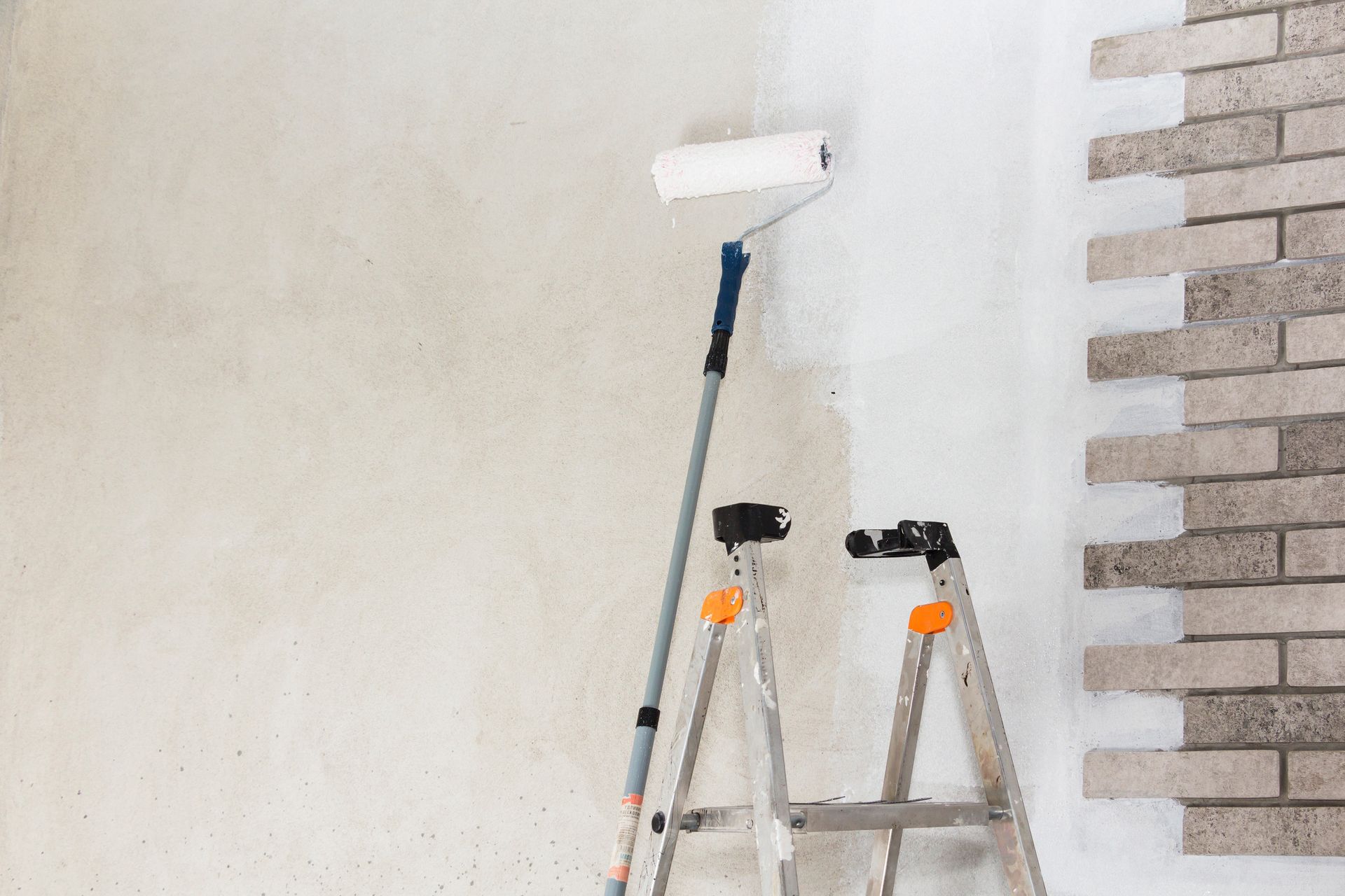Una escalera está junto a un rodillo de pintura en una pared.