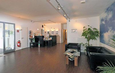 Moderne, offene Bürolounge mit schwarzen Sofas, Holzböden und einem Besprechungstisch in der Nähe großer Fenster.