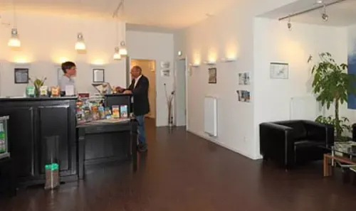 Moderne Lobby mit Rezeption, einem Mann, der mit Angestellten spricht, und schwarzen Sitzgelegenheiten entlang einer weißen Wand