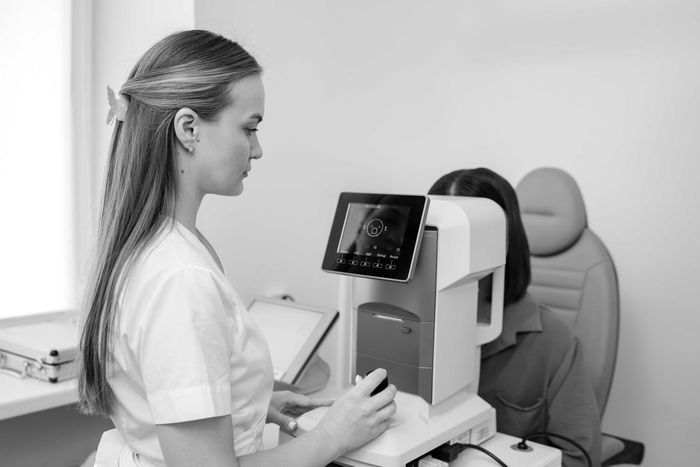 Techniker bedient ein Augenuntersuchungsgerät an einem sitzenden Patienten in einem Untersuchungsraum