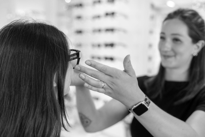 Zwei Personen in weißen Hemden unterhalten sich in einem hellen Optikergeschäft über Brillengestelle.