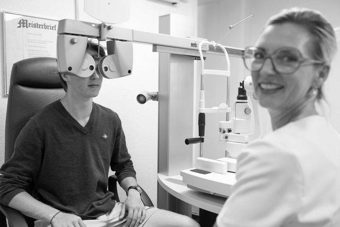 Optiker stellt in einer Klinik ein Augenuntersuchungsgerät für einen sitzenden Patienten ein.