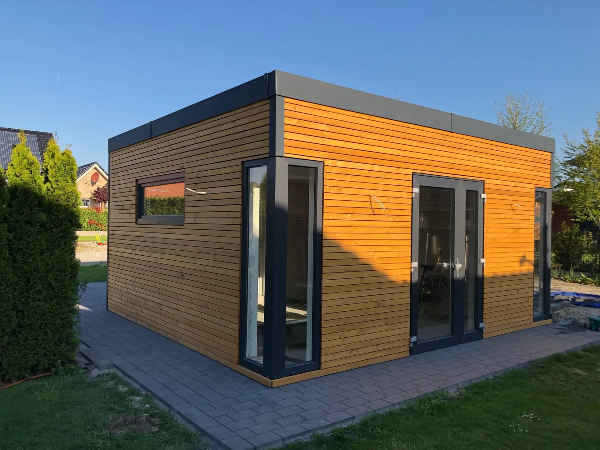 Ein kleines Holzhaus mit vielen Fenstern und Türen in einem Hinterhof.