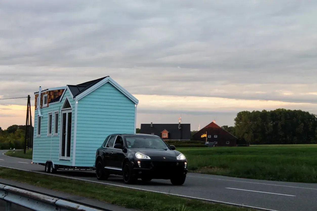 Ein Auto zieht ein kleines Haus auf einem Anhänger eine Straße entlang.