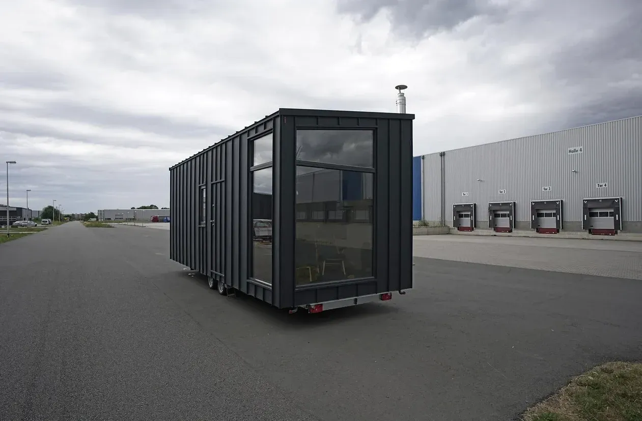 Ein schwarzer Anhänger fährt auf einer Straße vor einem Gebäude entlang.