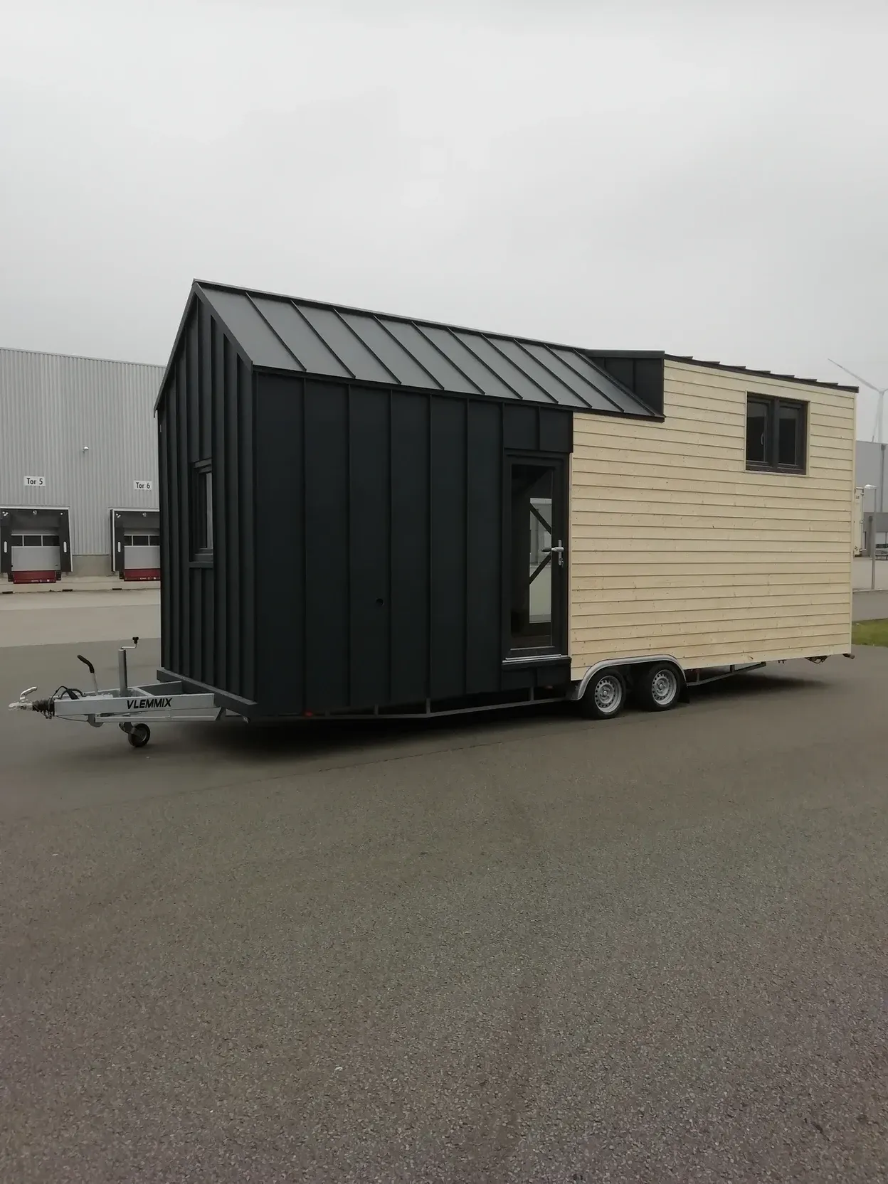 Auf einem Parkplatz steht ein kleines Haus auf einem Anhänger.