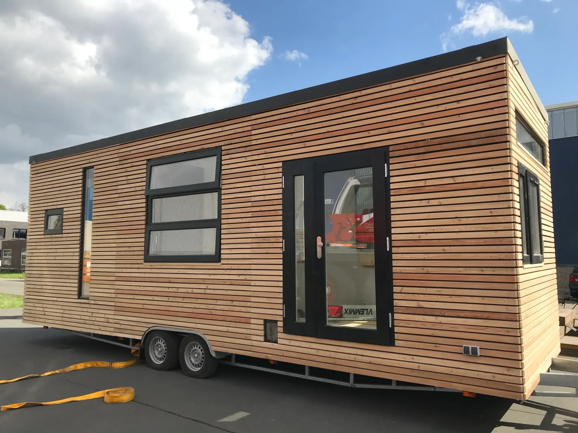 Auf einem Parkplatz steht ein kleines Haus auf Rädern.