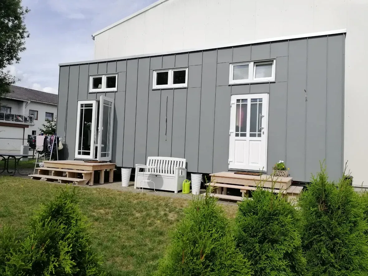 Ein kleines Haus mit einer Terrasse und einer Bank davor.