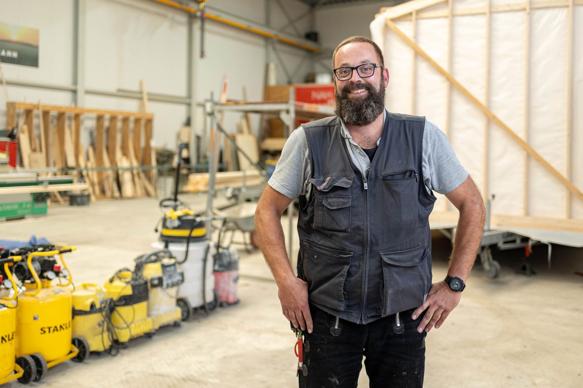 Ein Mann mit Bart steht mit den Händen in den Hüften in einer Lagerhalle.