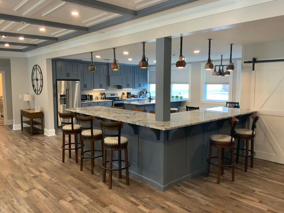 A spacious kitchen with a large island bar and wooden floors. Gray cabinetry and a white barn door are visible.