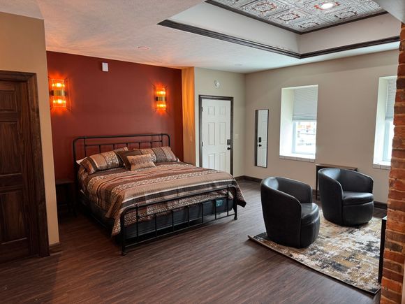 Bedroom with a dark bed frame, red accent wall, two black chairs, and decorative ceiling.