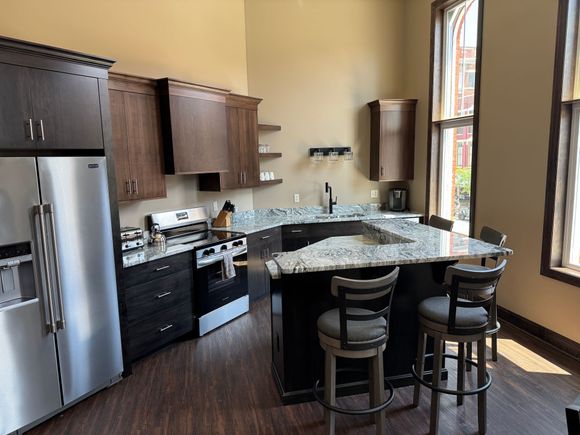 Kitchen with dark cabinets, stainless steel fridge, granite countertops, and a breakfast bar with stools.