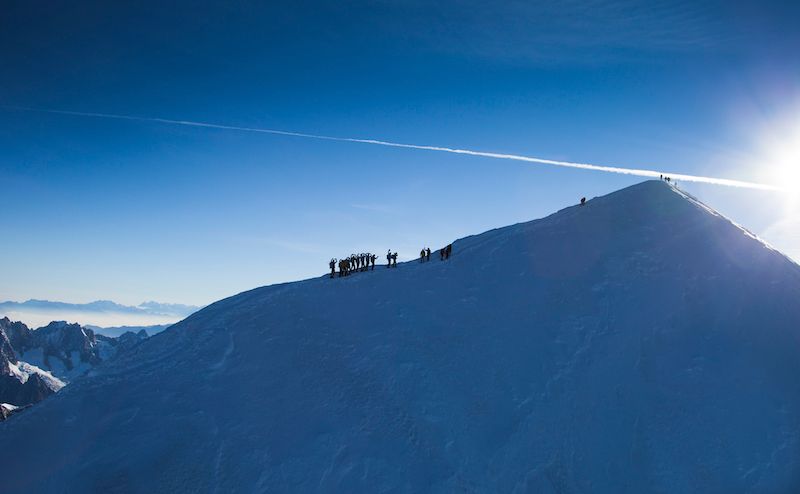 Snowy mountain peak with a group of people, under a bright blue sky.