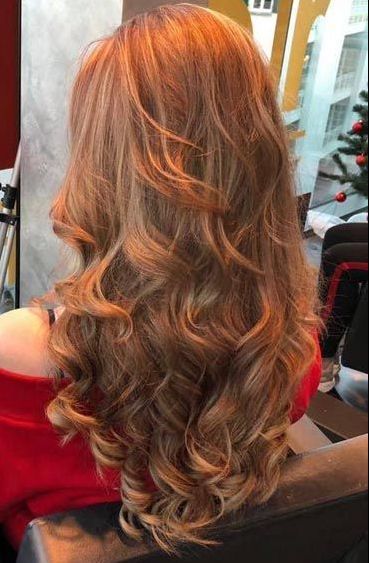 Eine Frau mit langen roten Haaren sitzt auf einem Stuhl vor einem Weihnachtsbaum.