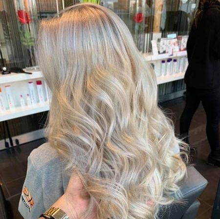 In einem Salon hält eine Person die blonden Haare einer Frau.