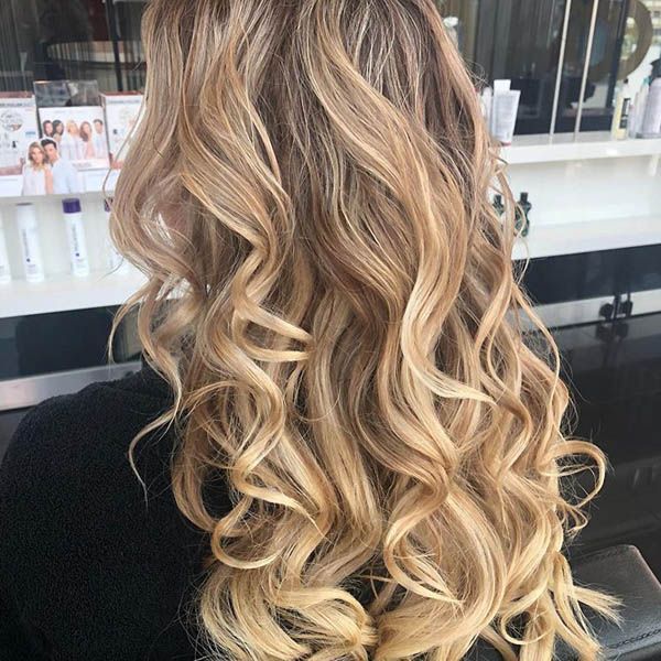 Eine Frau mit langen blonden Locken sitzt an einem Tisch.