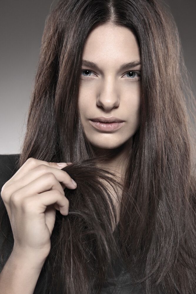 Eine Frau mit langen braunen Haaren hält ihr Haar in der Hand.