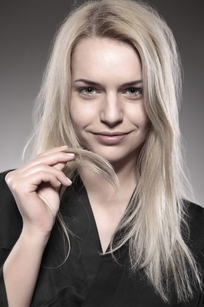 Eine Frau hält eine Haarsträhne und lächelt.