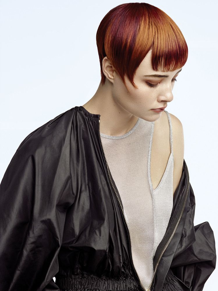 Eine Frau mit kurzen roten Haaren trägt eine schwarze Jacke und ein weißes Tanktop.