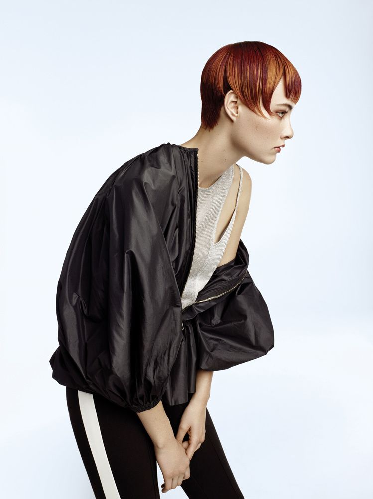 Eine Frau mit kurzen roten Haaren trägt eine schwarze Jacke und eine schwarze Hose.