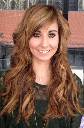 Eine Frau mit langen braunen Haaren lächelt und trägt einen grünen Pullover.