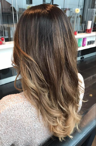 Eine Frau mit langen braunen Haaren sitzt auf einem Stuhl in einem Salon.