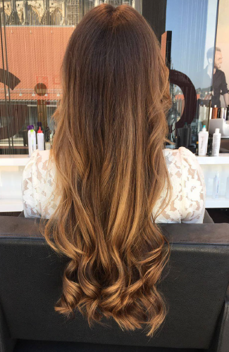 Eine Frau mit langen braunen Haaren sitzt auf einem Stuhl in einem Salon.