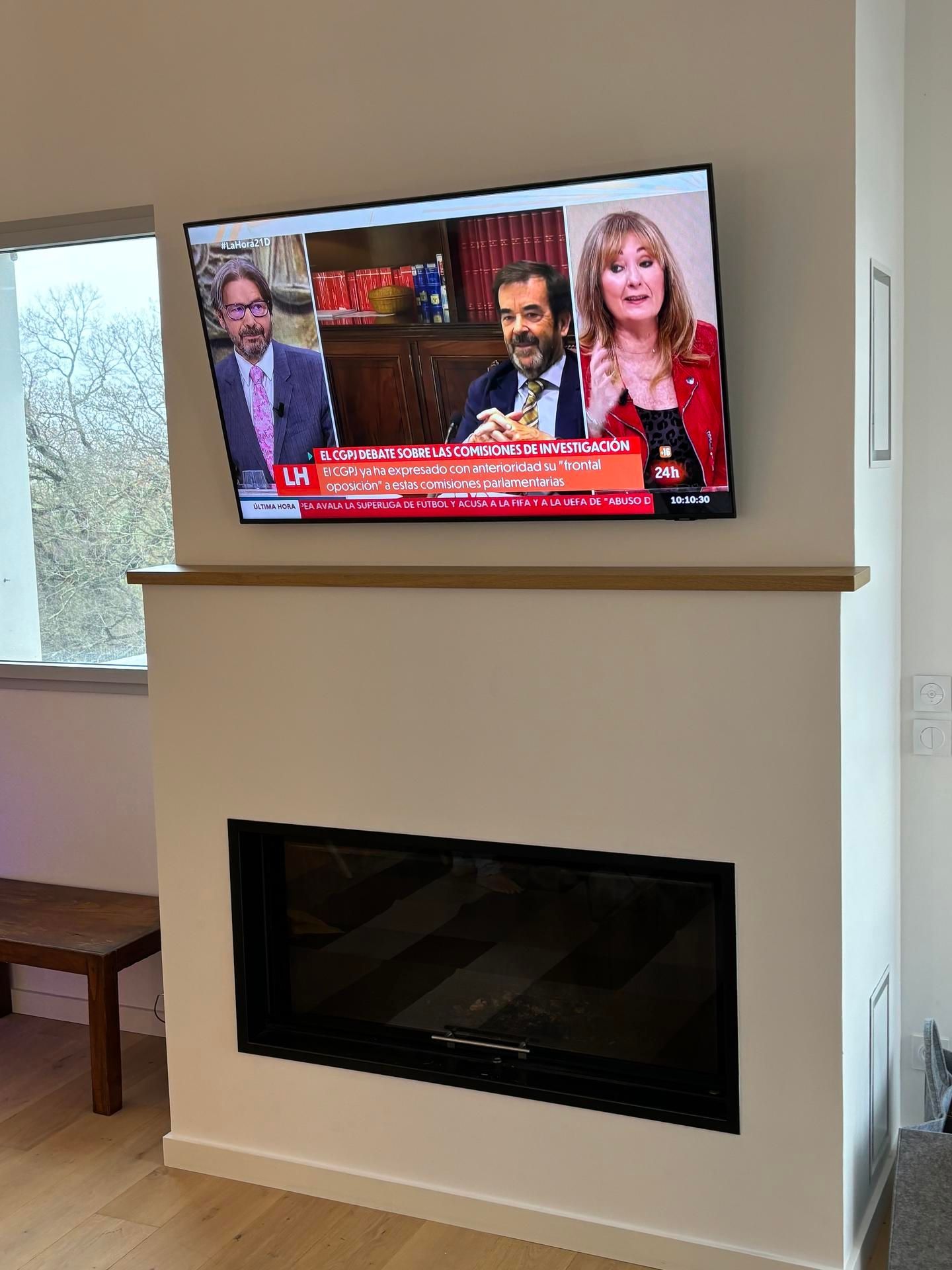 Téléviseur mural au-dessus d'une cheminée moderne dans un salon lumineux, diffusant un journal télévisé.