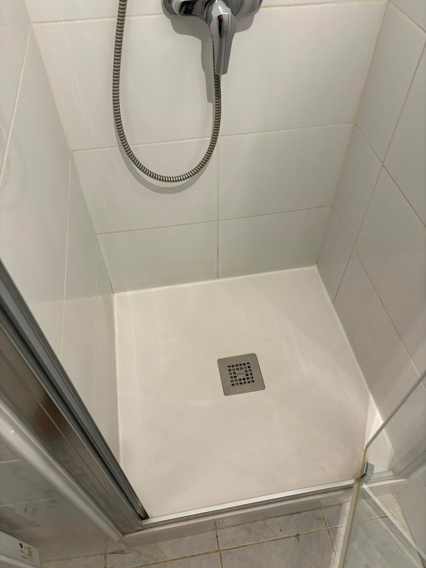 Petite douche carrelée avec pommeau de douche à main et bonde de sol carrée.