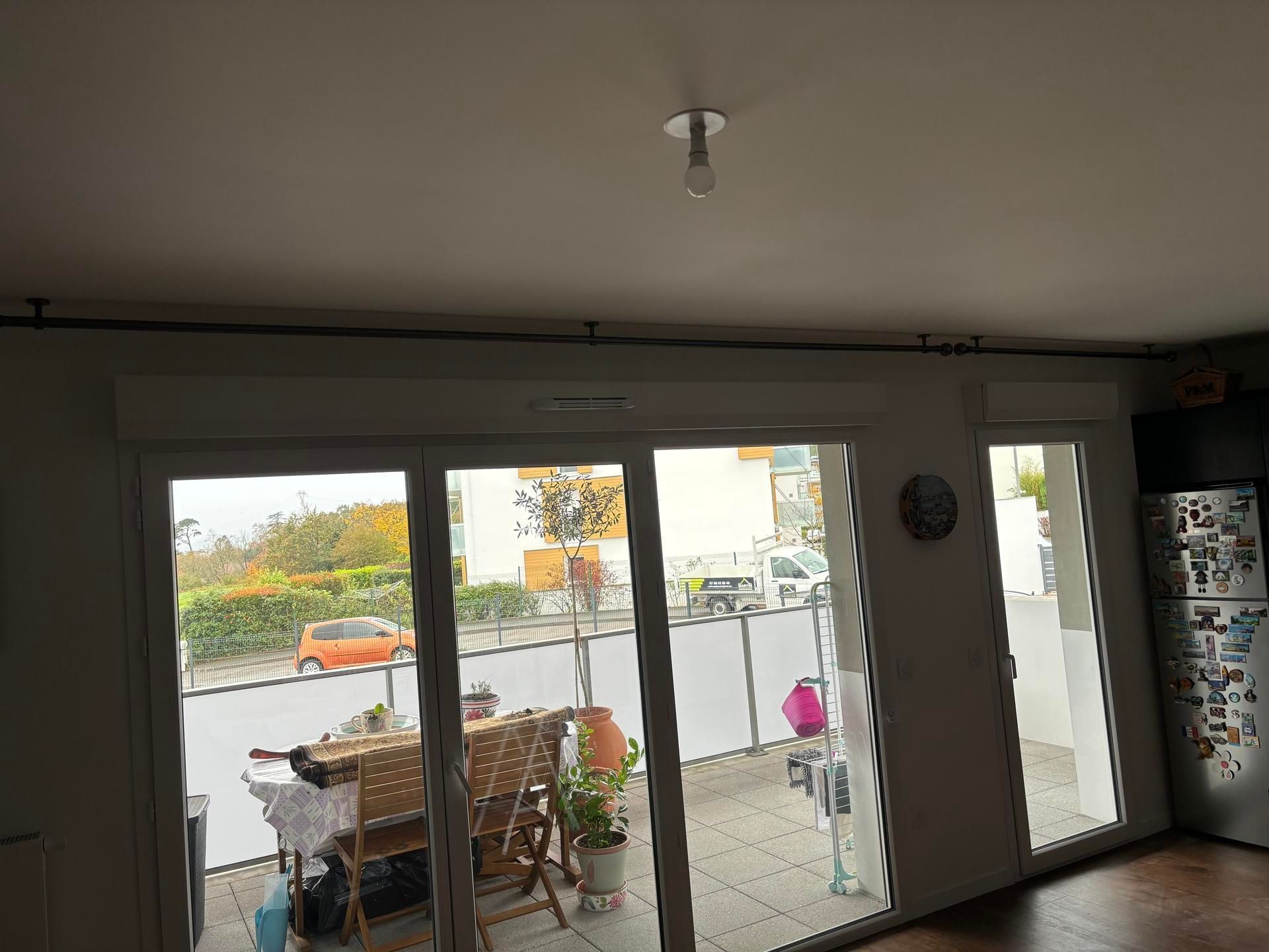 Salon avec de grandes portes coulissantes en verre donnant sur une terrasse et une vue sur la rue.