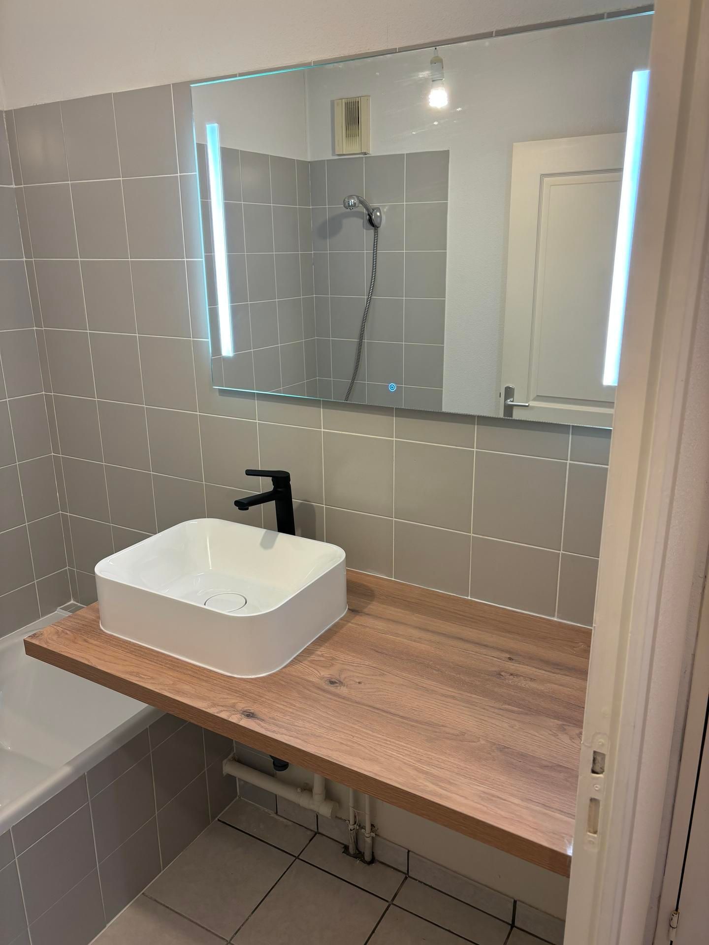 Meuble moderne sous lavabo avec comptoir en bois, vasque blanche, robinet noir et armoire à miroir.