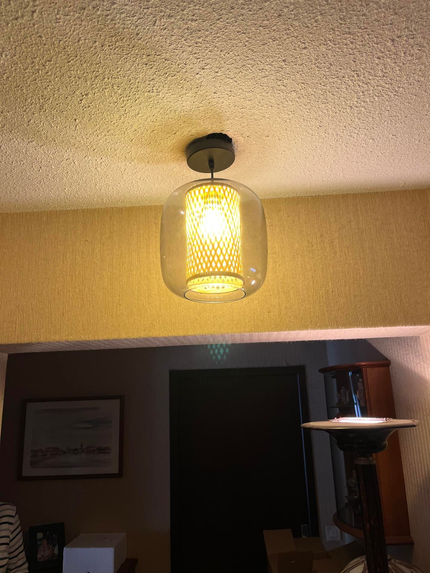 Un plafonnier avec un abat-jour en verre texturé éclaire l'embrasure d'une porte, avec un lampadaire en dessous.