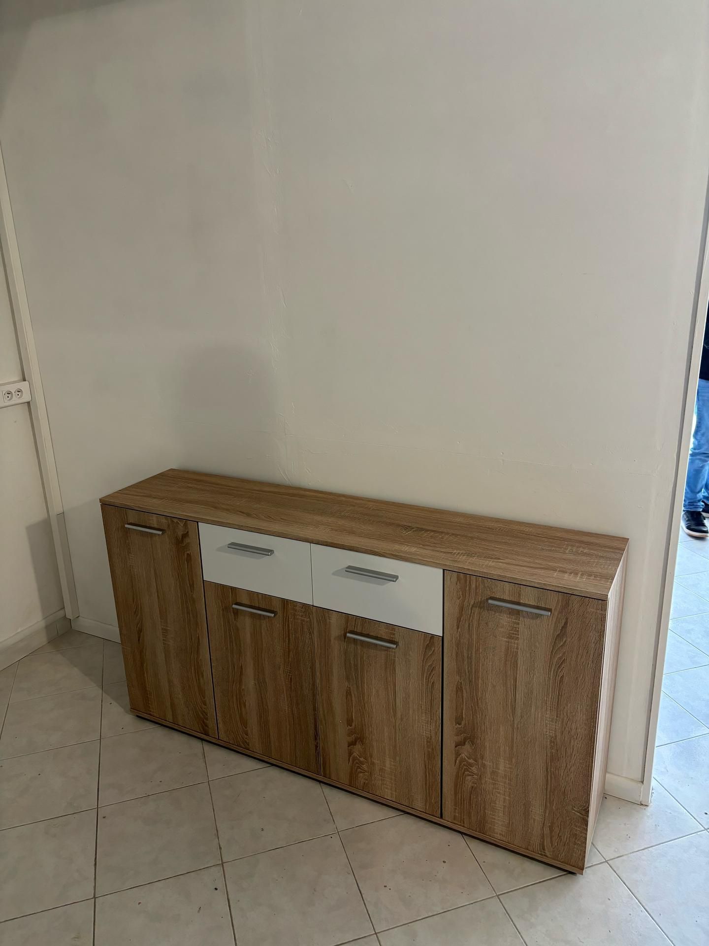 Meuble de rangement en bois avec tiroirs blancs contre un mur clair sur un sol carrelé.