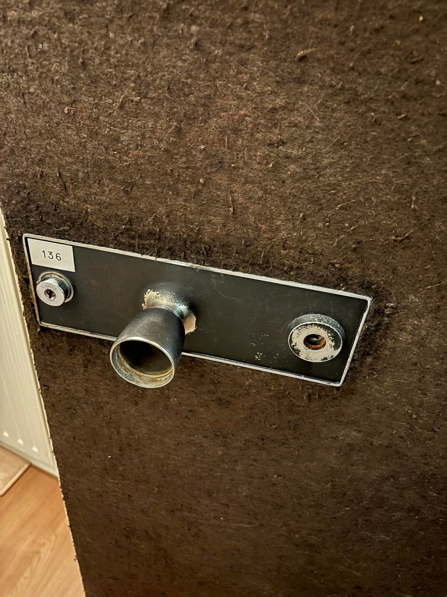 Gros plan sur une plaque de fixation murale en métal comportant deux ouvertures circulaires, sur un mur texturé brun.