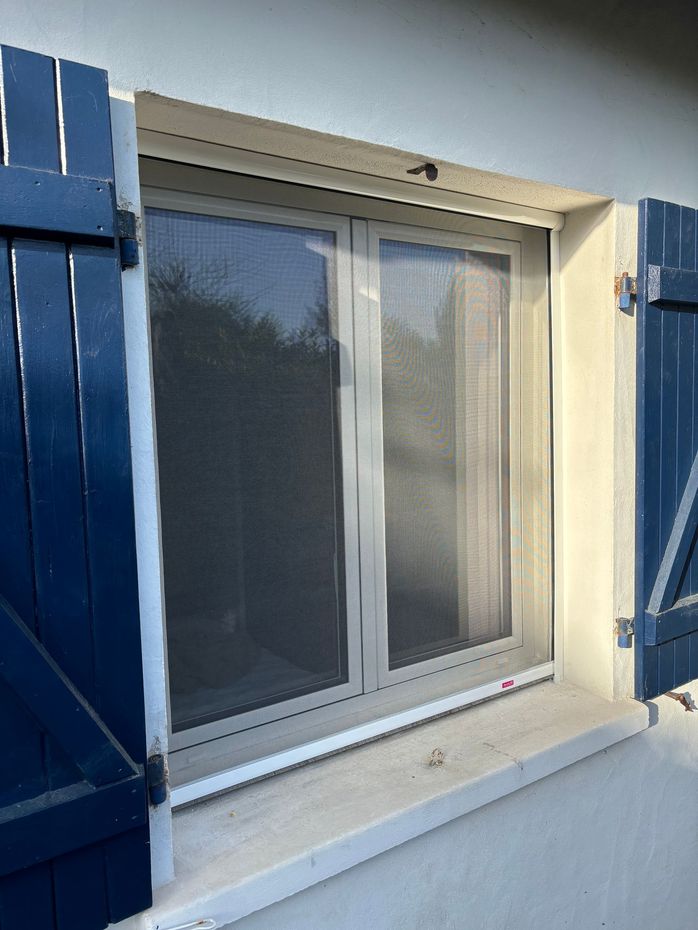 Fenêtre coulissante blanche avec volets bleus sur l'extérieur d'une maison.