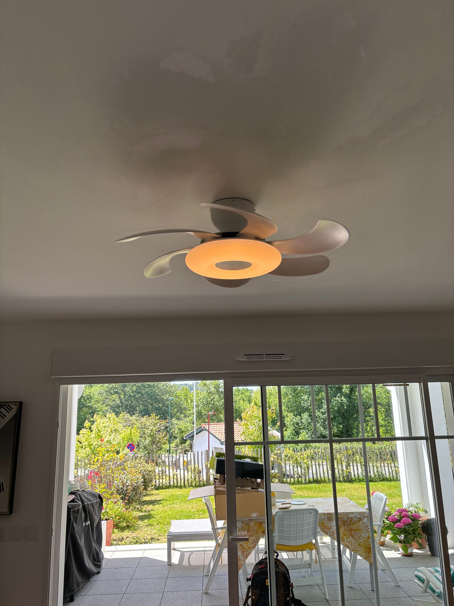 Salon avec ventilateur de plafond et porte-fenêtre coulissante donnant sur une terrasse et un jardin.