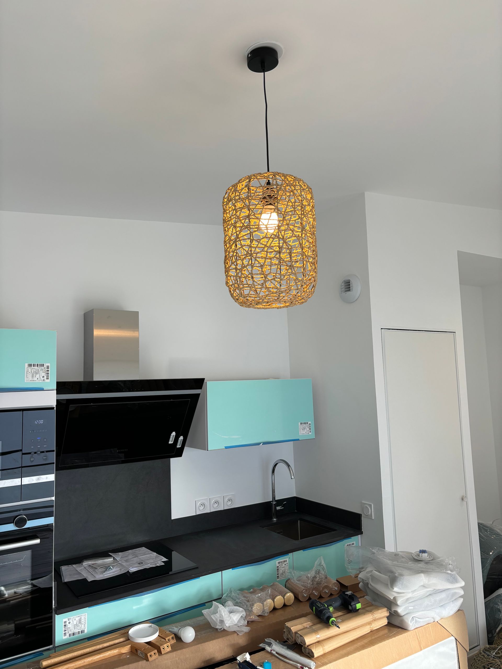 Cuisine moderne avec comptoirs noirs, armoires vert menthe et suspension lumineuse en tissu tressé au-dessus de l'îlot.