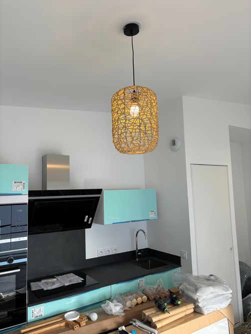 Cuisine moderne avec comptoirs noirs, armoires vert menthe et suspension lumineuse en tissu tressé au-dessus de l'îlot.