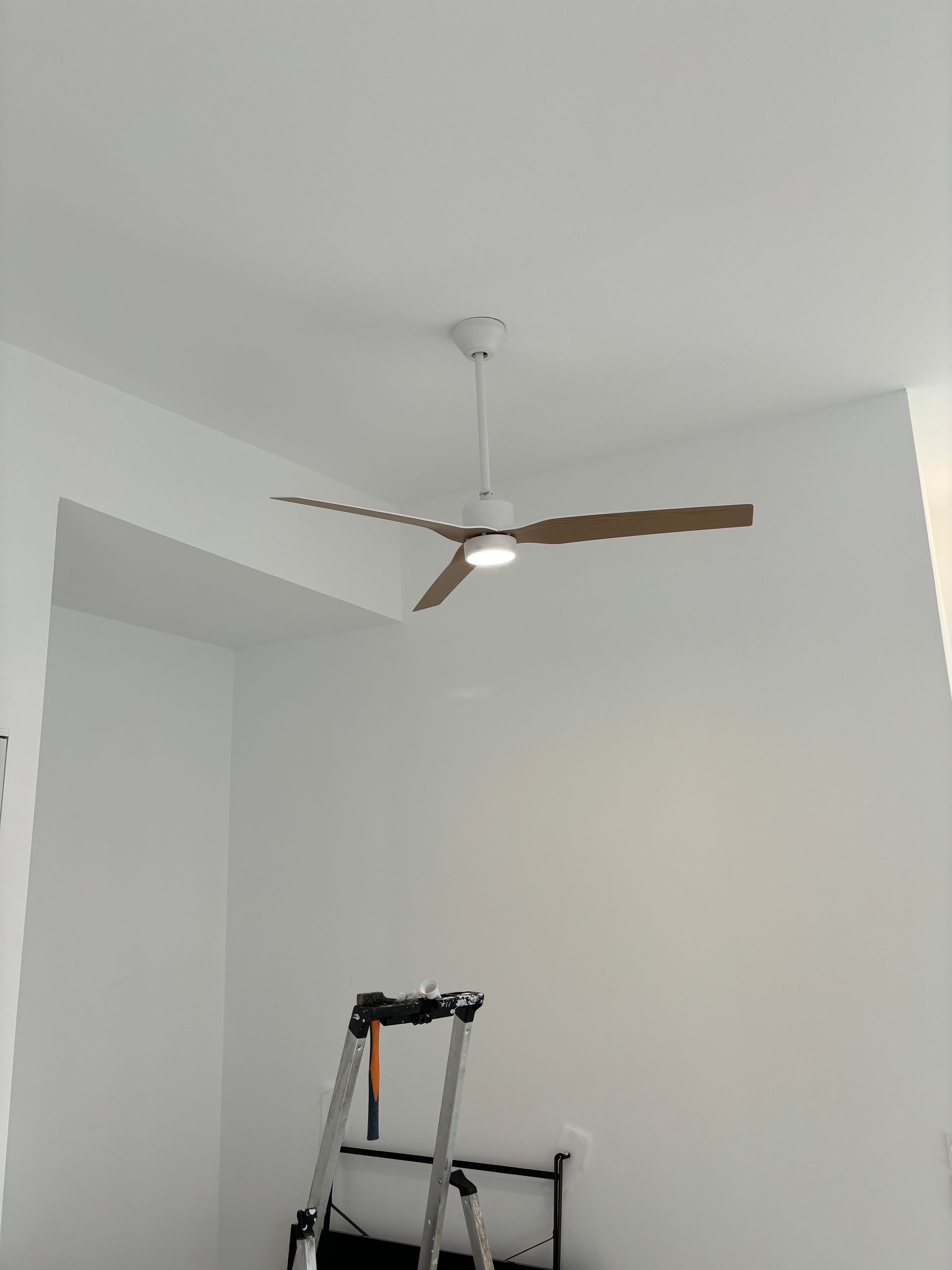 Chambre blanche avec un ventilateur de plafond et un déambulateur ou un tabouret pliant près du mur.